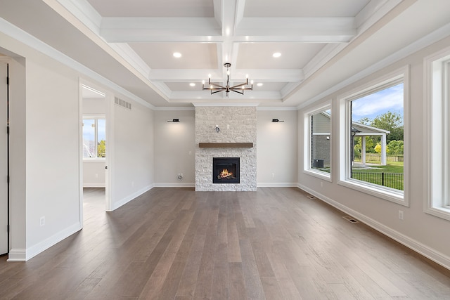 unfurnished living room with crown molding, beam ceiling, a chandelier, hardwood / wood-style floors, and a stone fireplace