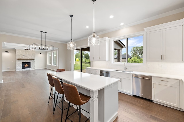 kitchen with a stone fireplace, sink, white cabinets, and stainless steel dishwasher