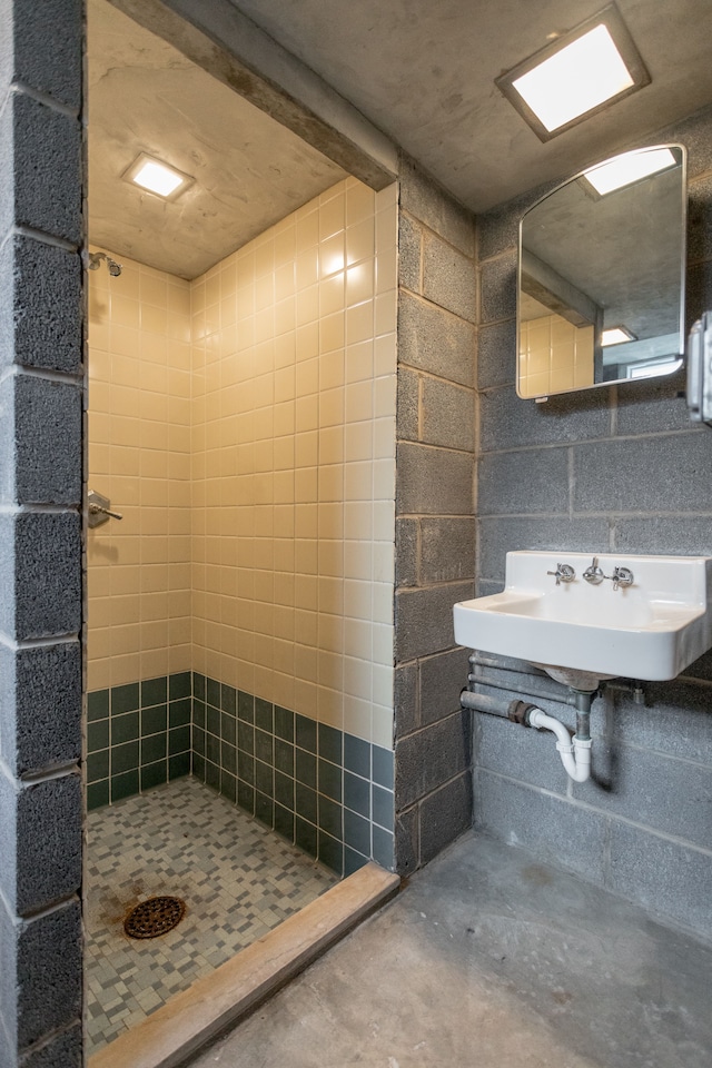 bathroom with concrete flooring, tiled shower, and sink