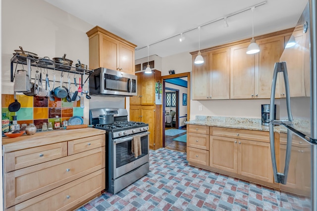 kitchen featuring light stone countertops, track lighting, stainless steel appliances, light brown cabinets, and decorative light fixtures