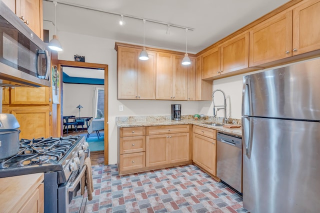 kitchen with appliances with stainless steel finishes, track lighting, light stone counters, sink, and hanging light fixtures