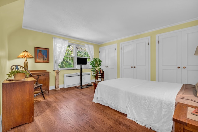 bedroom with radiator heating unit, ornamental molding, two closets, and light wood-type flooring