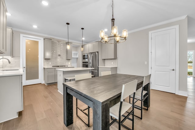 kitchen with hanging light fixtures, appliances with stainless steel finishes, gray cabinets, a kitchen island, and light wood-type flooring