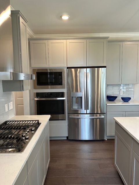 kitchen with gray cabinetry, dark wood-type flooring, wall chimney exhaust hood, decorative backsplash, and appliances with stainless steel finishes