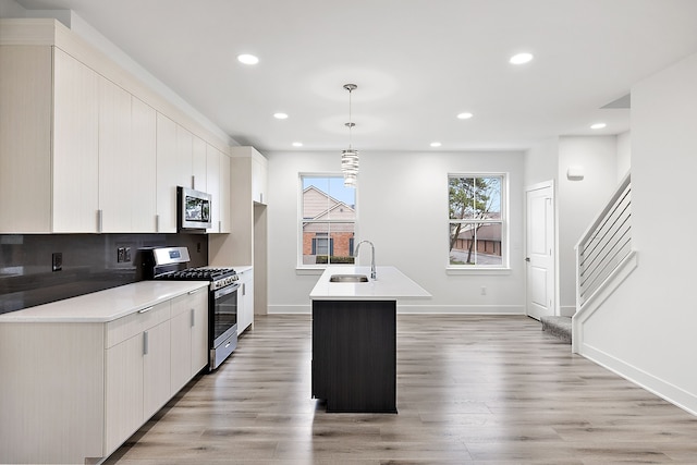 kitchen featuring stainless steel appliances, a kitchen island with sink, sink, decorative light fixtures, and light hardwood / wood-style floors