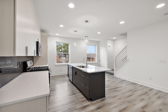 kitchen with white cabinets, sink, an island with sink, appliances with stainless steel finishes, and decorative light fixtures