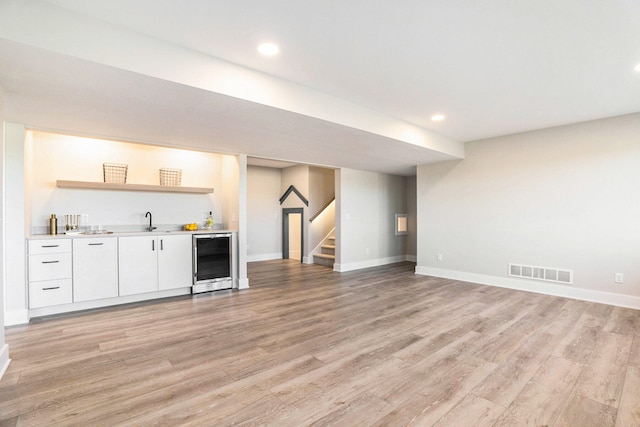 bar with light wood-type flooring, wine cooler, white cabinetry, and sink