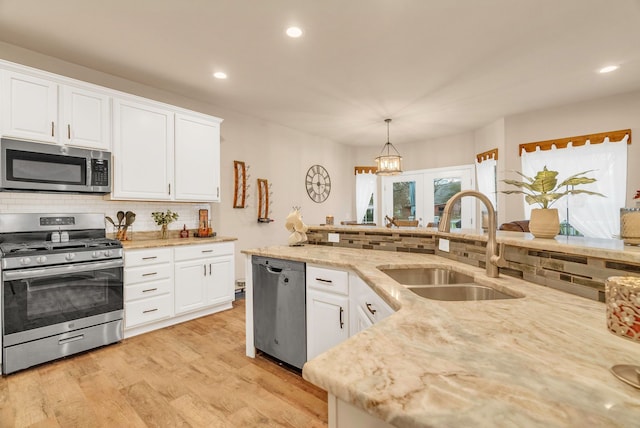 kitchen featuring white cabinetry, sink, stainless steel appliances, pendant lighting, and light wood-type flooring