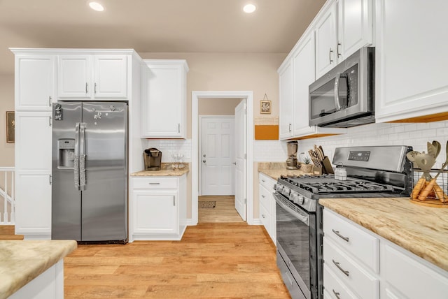 kitchen featuring white cabinetry, light stone countertops, stainless steel appliances, light hardwood / wood-style flooring, and backsplash