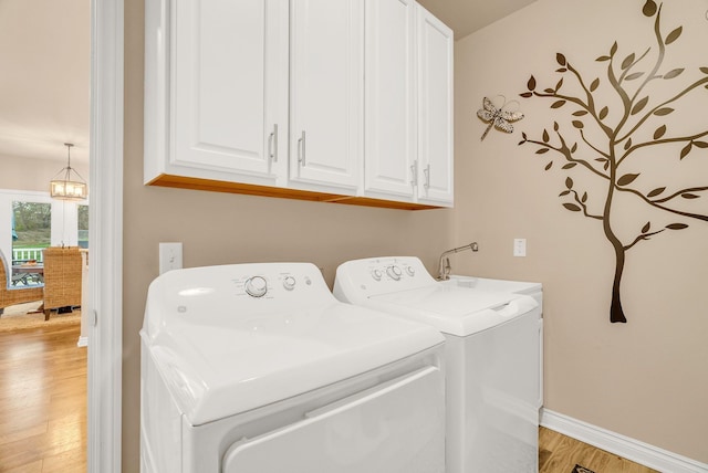 clothes washing area featuring cabinets, washer and dryer, a notable chandelier, and light wood-type flooring