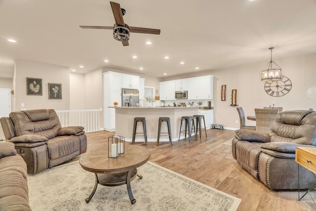 living room featuring ceiling fan with notable chandelier and light hardwood / wood-style floors