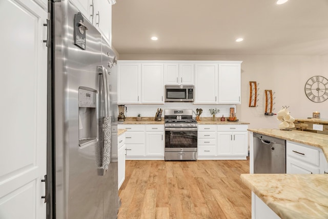 kitchen with appliances with stainless steel finishes, tasteful backsplash, light stone counters, light hardwood / wood-style floors, and white cabinetry