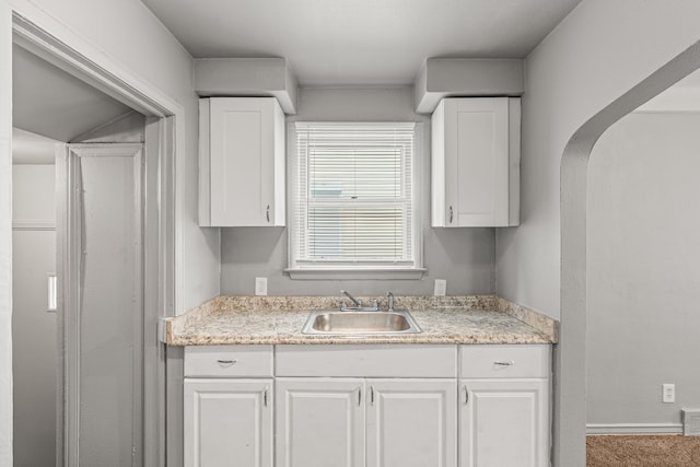 kitchen with white cabinetry, sink, and carpet