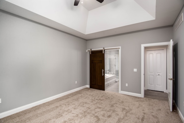 unfurnished bedroom featuring carpet, ceiling fan, a barn door, and connected bathroom