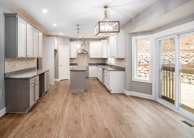 kitchen featuring a healthy amount of sunlight, a kitchen island, wall chimney range hood, and hanging light fixtures