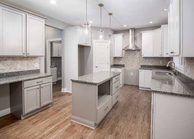 kitchen with white cabinets, a center island, wall chimney exhaust hood, and sink