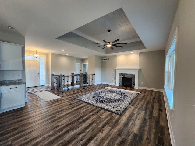 unfurnished living room with a healthy amount of sunlight, dark hardwood / wood-style flooring, a tray ceiling, a fireplace, and ceiling fan with notable chandelier