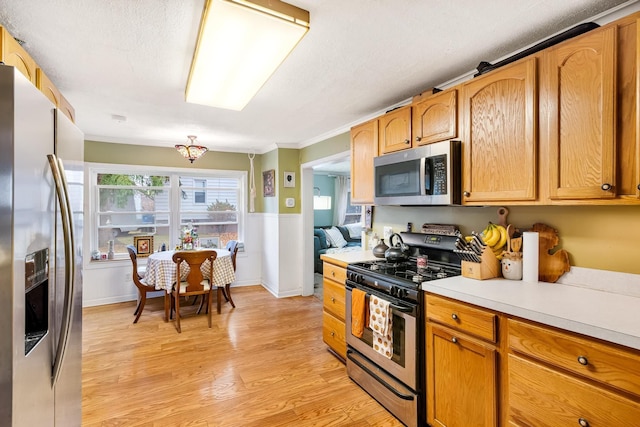 kitchen featuring crown molding, light hardwood / wood-style floors, a textured ceiling, and appliances with stainless steel finishes