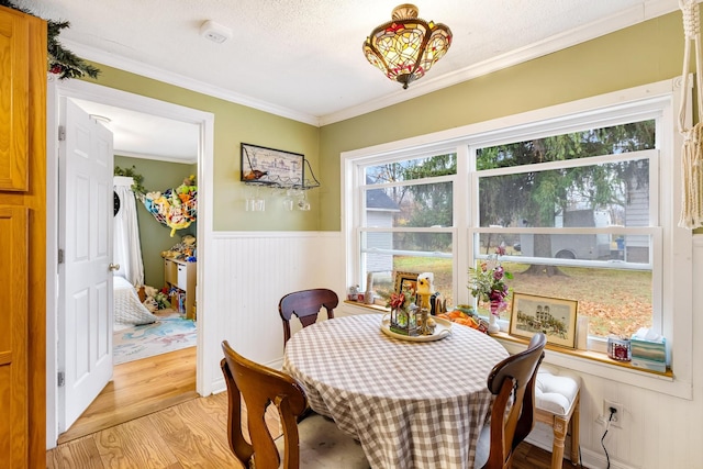 dining room with a textured ceiling, light wood-type flooring, wooden walls, and crown molding