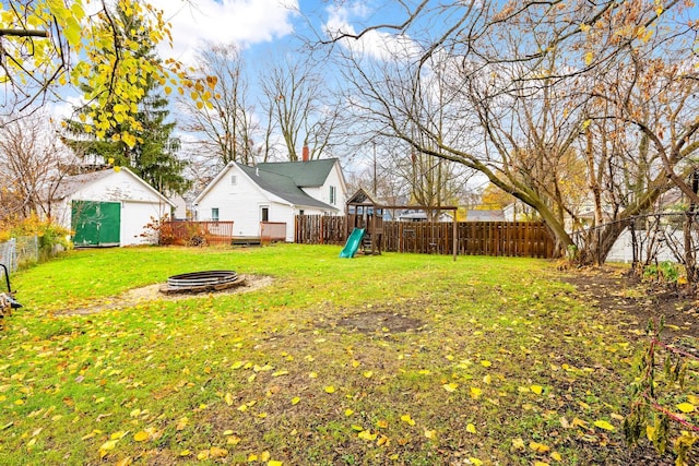 view of yard with a playground, a storage unit, a deck, and an outdoor fire pit