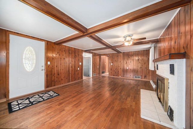 unfurnished living room featuring coffered ceiling, wooden walls, light hardwood / wood-style flooring, ceiling fan, and beam ceiling