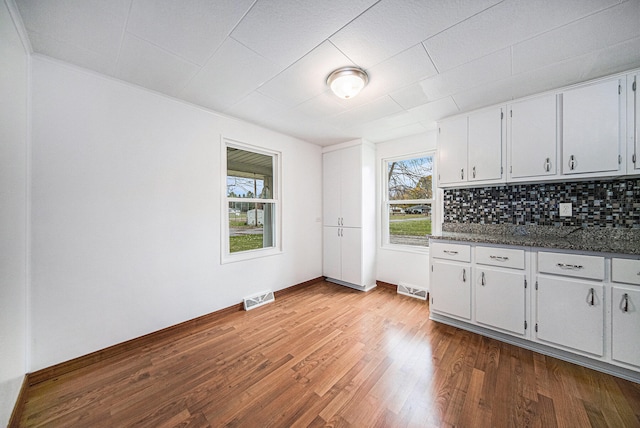 kitchen with hardwood / wood-style floors, white cabinets, decorative backsplash, dark stone countertops, and ornamental molding