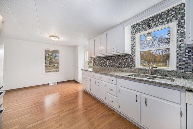 kitchen featuring backsplash, sink, light hardwood / wood-style flooring, dark stone countertops, and hanging light fixtures