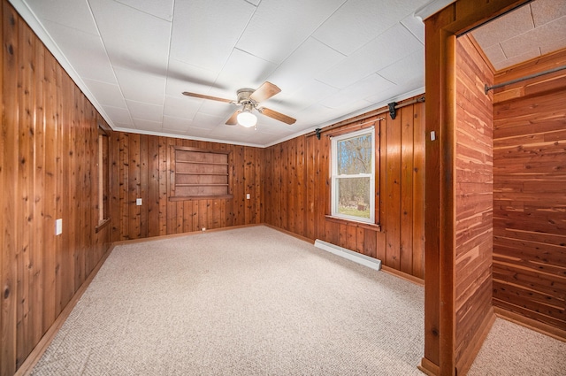 carpeted spare room with wood walls, ceiling fan, and a baseboard radiator