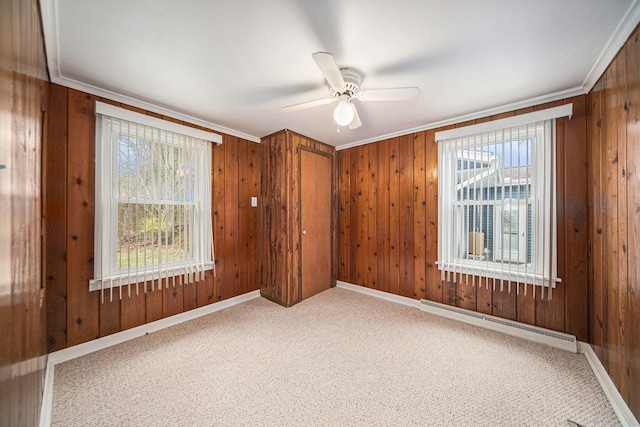 carpeted empty room featuring crown molding, ceiling fan, a baseboard heating unit, and wood walls