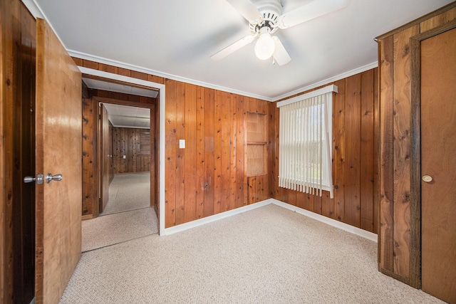 unfurnished bedroom with carpet flooring, ceiling fan, wooden walls, and ornamental molding