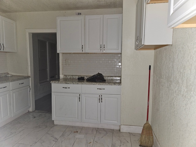 kitchen with backsplash, white cabinetry, dark stone counters, and a textured ceiling