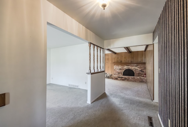 unfurnished living room featuring beamed ceiling, carpet floors, a fireplace, and wood walls