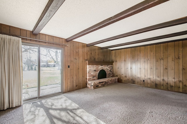 unfurnished living room featuring a fireplace, a textured ceiling, beamed ceiling, carpet floors, and wood walls