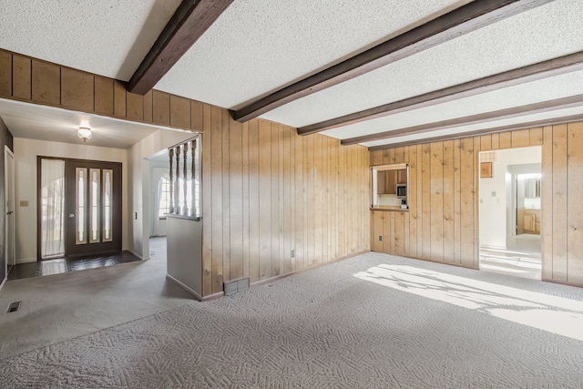 interior space with wood walls, beam ceiling, a textured ceiling, and carpet