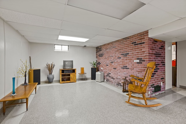 living area with brick wall, tile patterned floors, a paneled ceiling, and baseboards