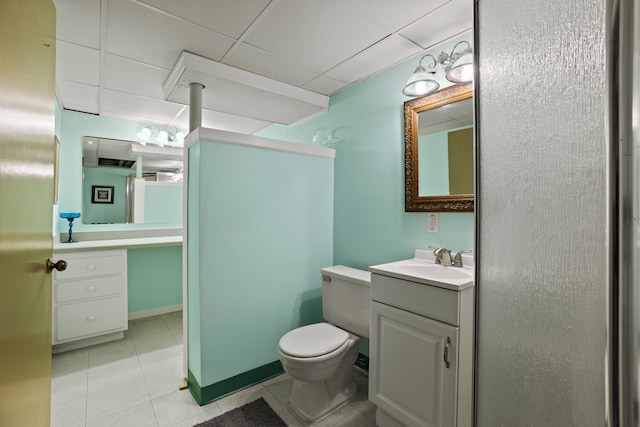 bathroom with baseboards, a drop ceiling, toilet, tile patterned floors, and vanity