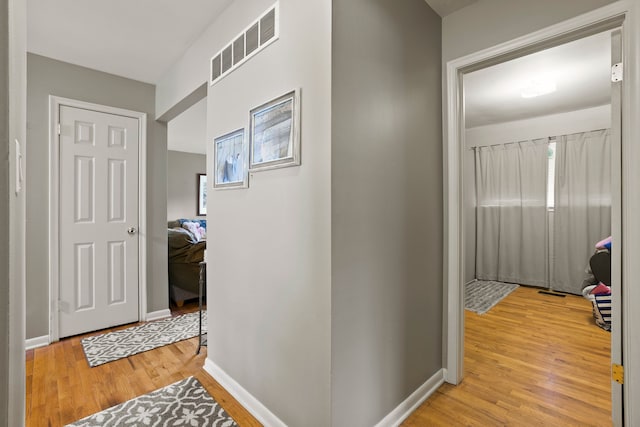 hallway with light wood-style floors, baseboards, and visible vents