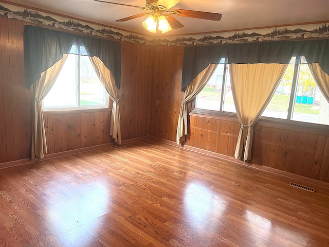 empty room with wooden walls, ceiling fan, and hardwood / wood-style flooring