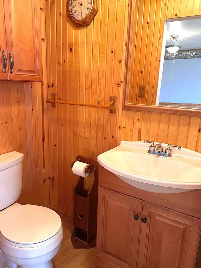 bathroom with vanity, toilet, wood-type flooring, and wooden walls