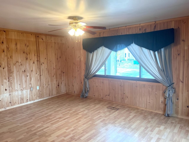 empty room featuring wood walls, ceiling fan, and light wood-type flooring