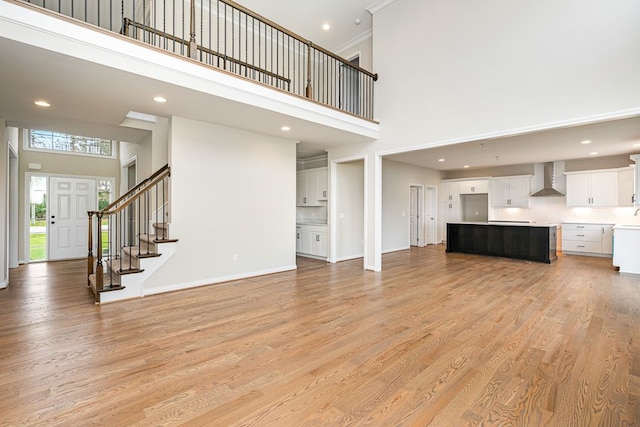 unfurnished living room featuring light wood-type flooring, a towering ceiling, and crown molding