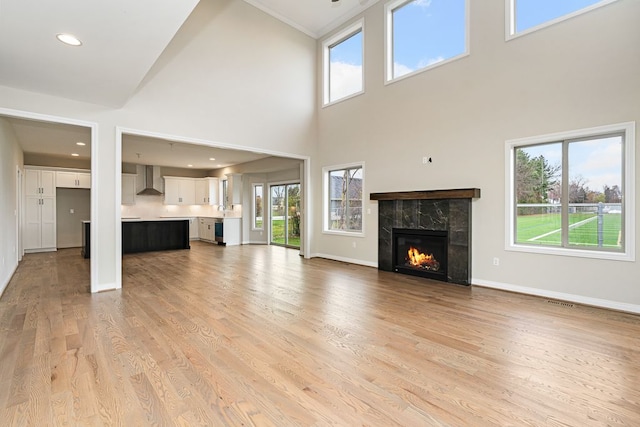 unfurnished living room featuring a premium fireplace, a high ceiling, a wealth of natural light, and light hardwood / wood-style flooring