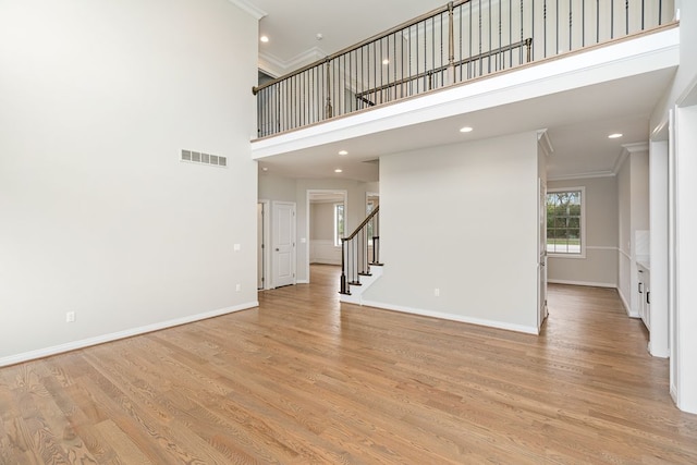 unfurnished living room featuring a towering ceiling, light hardwood / wood-style floors, and ornamental molding