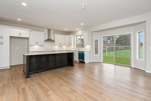 kitchen with white cabinets, a center island, wall chimney exhaust hood, and light wood-type flooring