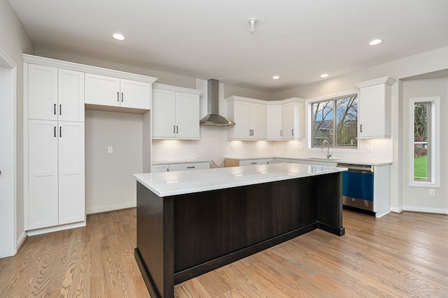 kitchen with wall chimney exhaust hood, dishwasher, a center island, light hardwood / wood-style floors, and white cabinetry