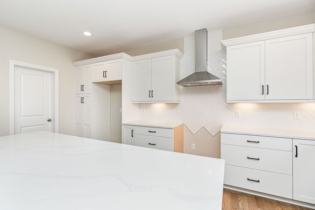 kitchen with decorative backsplash, white cabinetry, wall chimney range hood, and light wood-type flooring