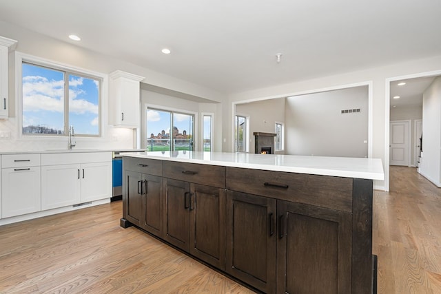 kitchen featuring dishwasher, sink, a kitchen island, light hardwood / wood-style floors, and white cabinets