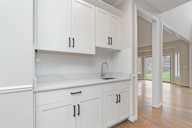 kitchen featuring sink, decorative backsplash, light hardwood / wood-style floors, light stone counters, and white cabinetry