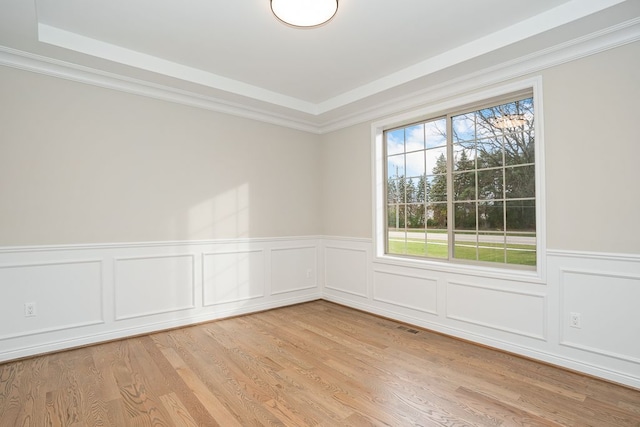 unfurnished room featuring light hardwood / wood-style floors, a raised ceiling, and ornamental molding