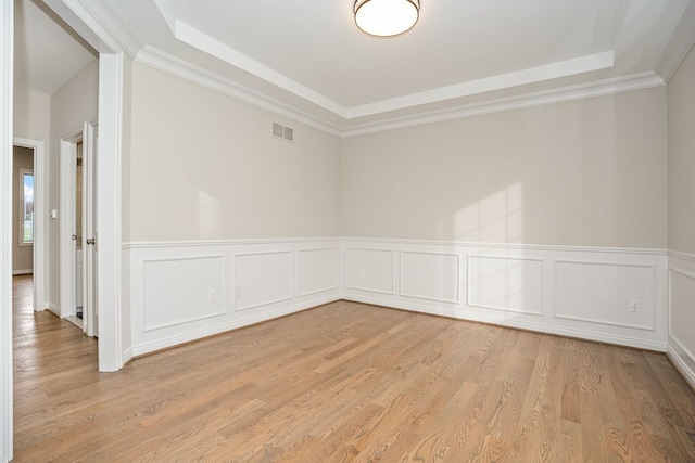 spare room featuring a tray ceiling, crown molding, and light hardwood / wood-style flooring